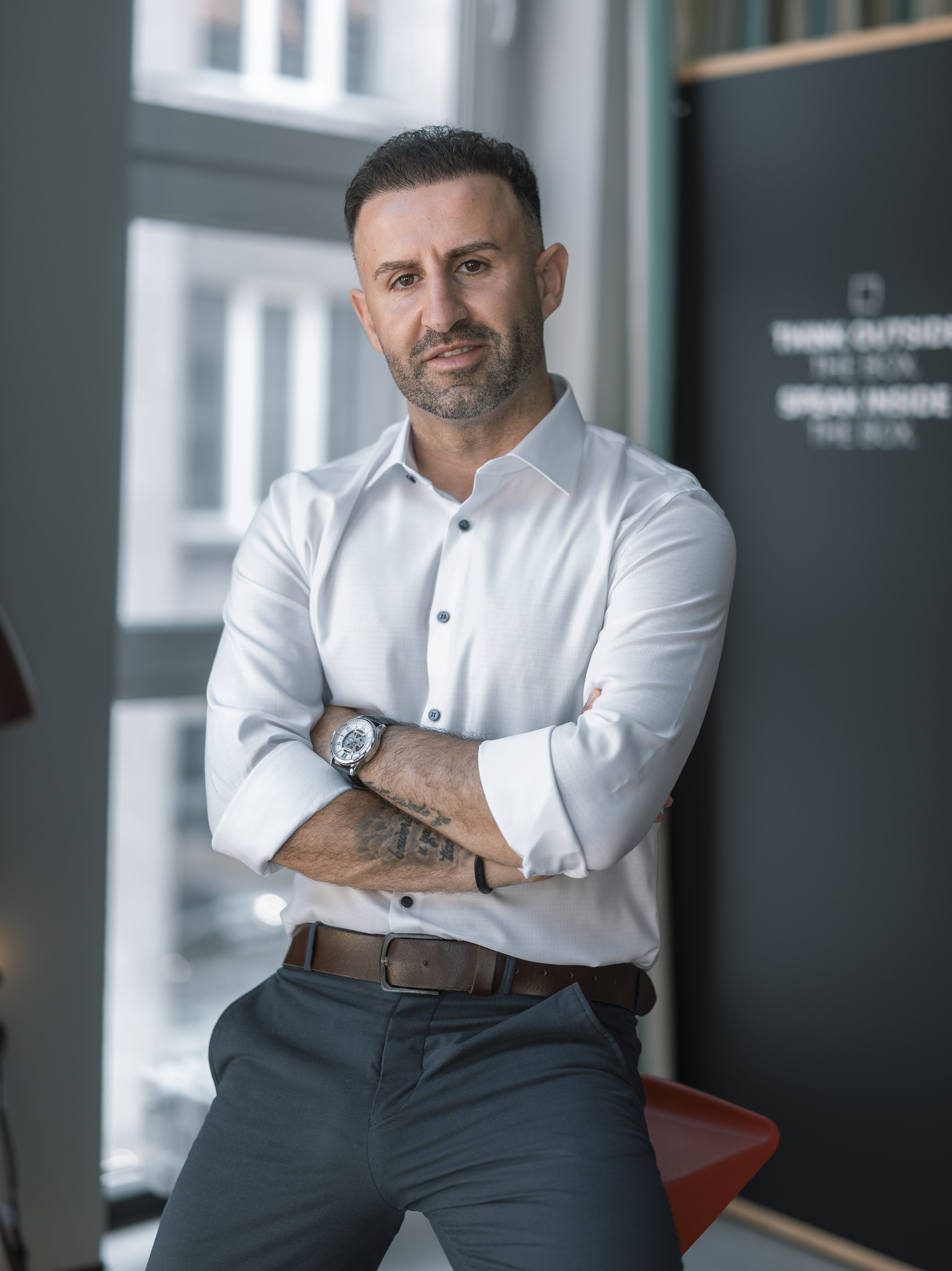 Mann im Business Outfit steht mit verschränkten Armen in einem modernen Raum